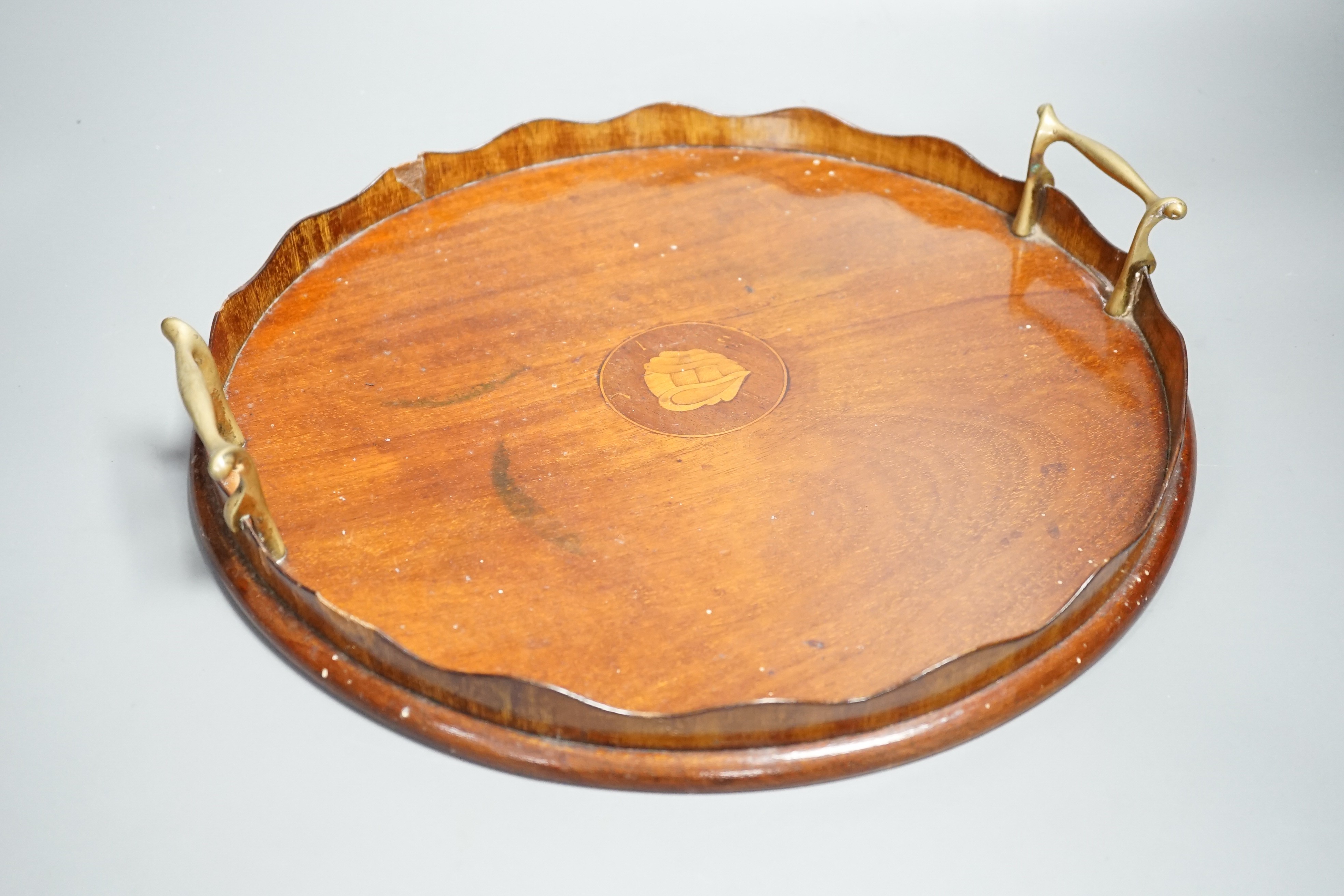 A circular shell inlaid, pie crust edged, brass handled, mahogany tray, 34.5 cms diameter